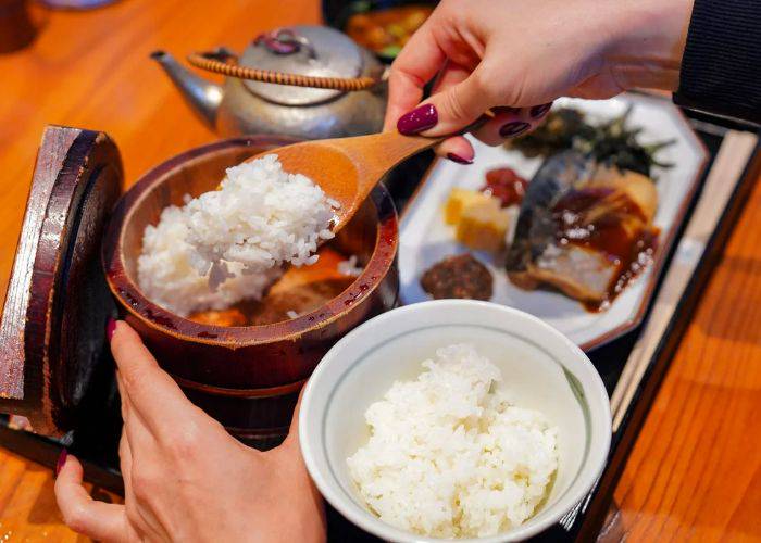 Someone serving sticky rice at a traditional Japanese breakfast experience.